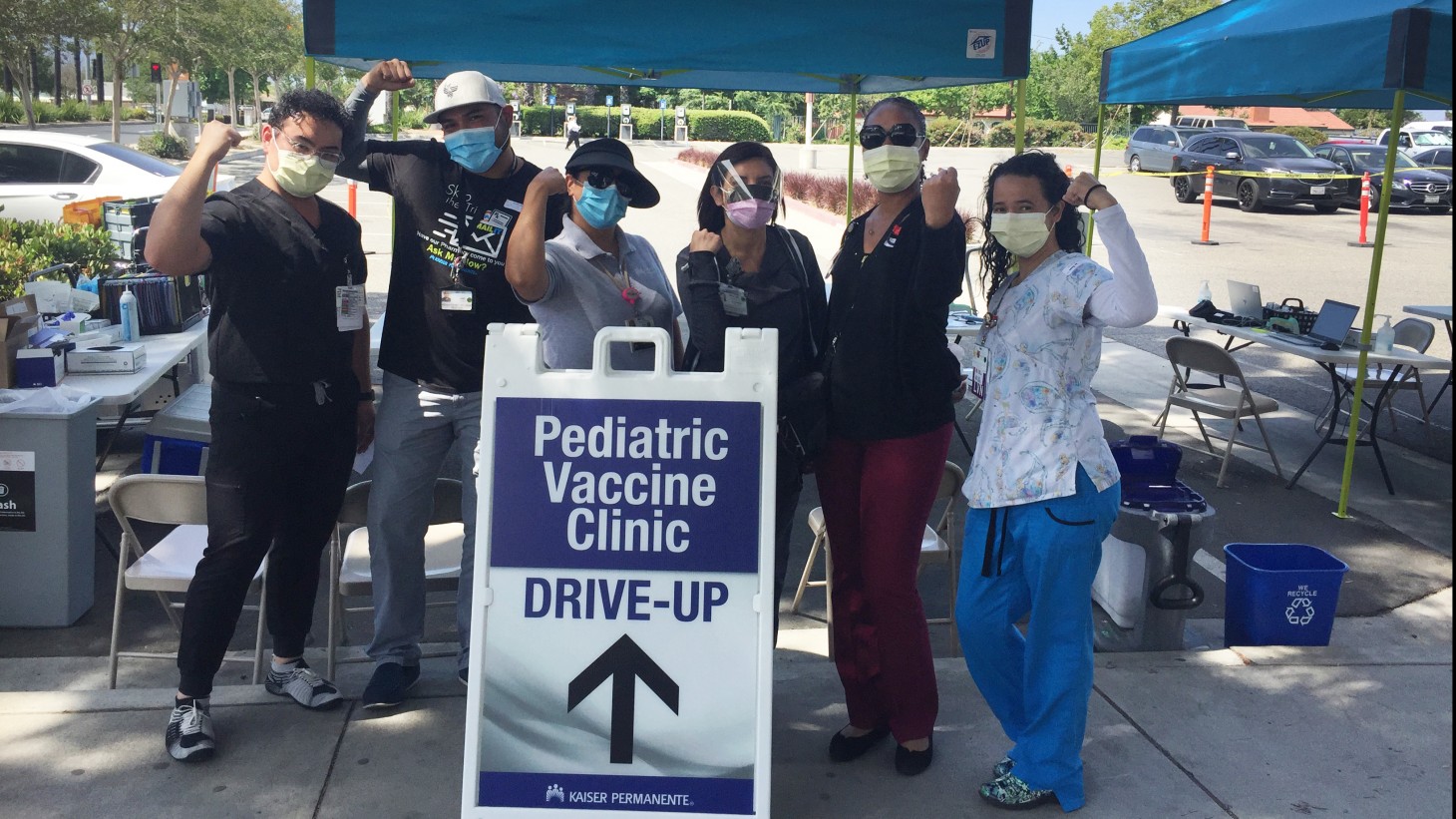 a group of health care workers, outdoors, flexing their muscles