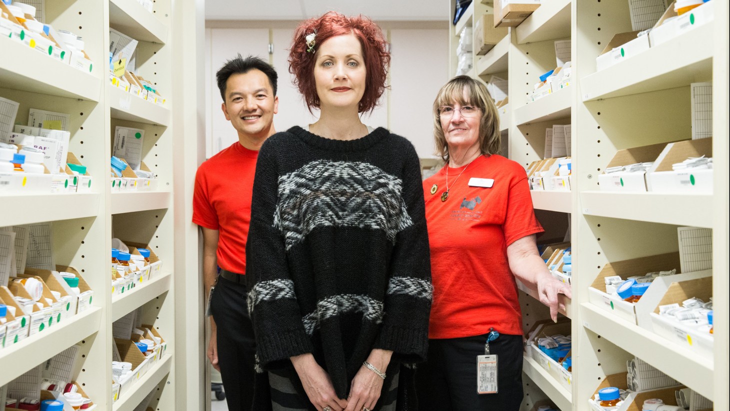 Three people standing amid shelves of pharmacy supplies 