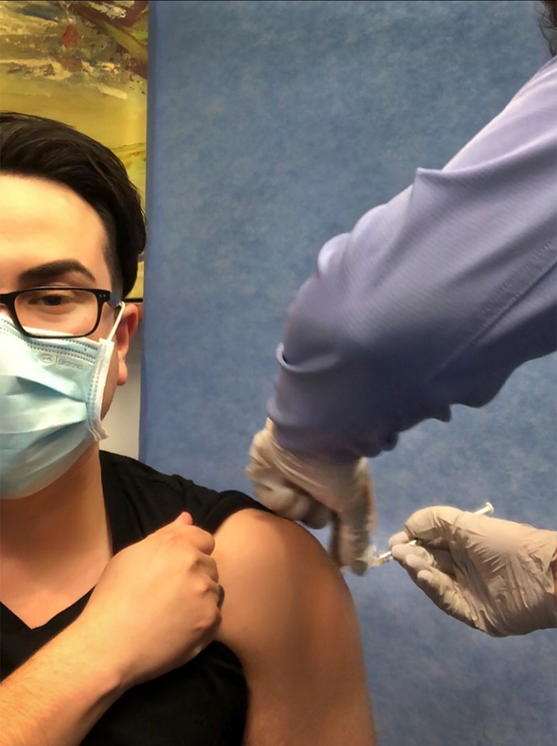 Photo of a young man, wearing a mask, getting a vaccine. 