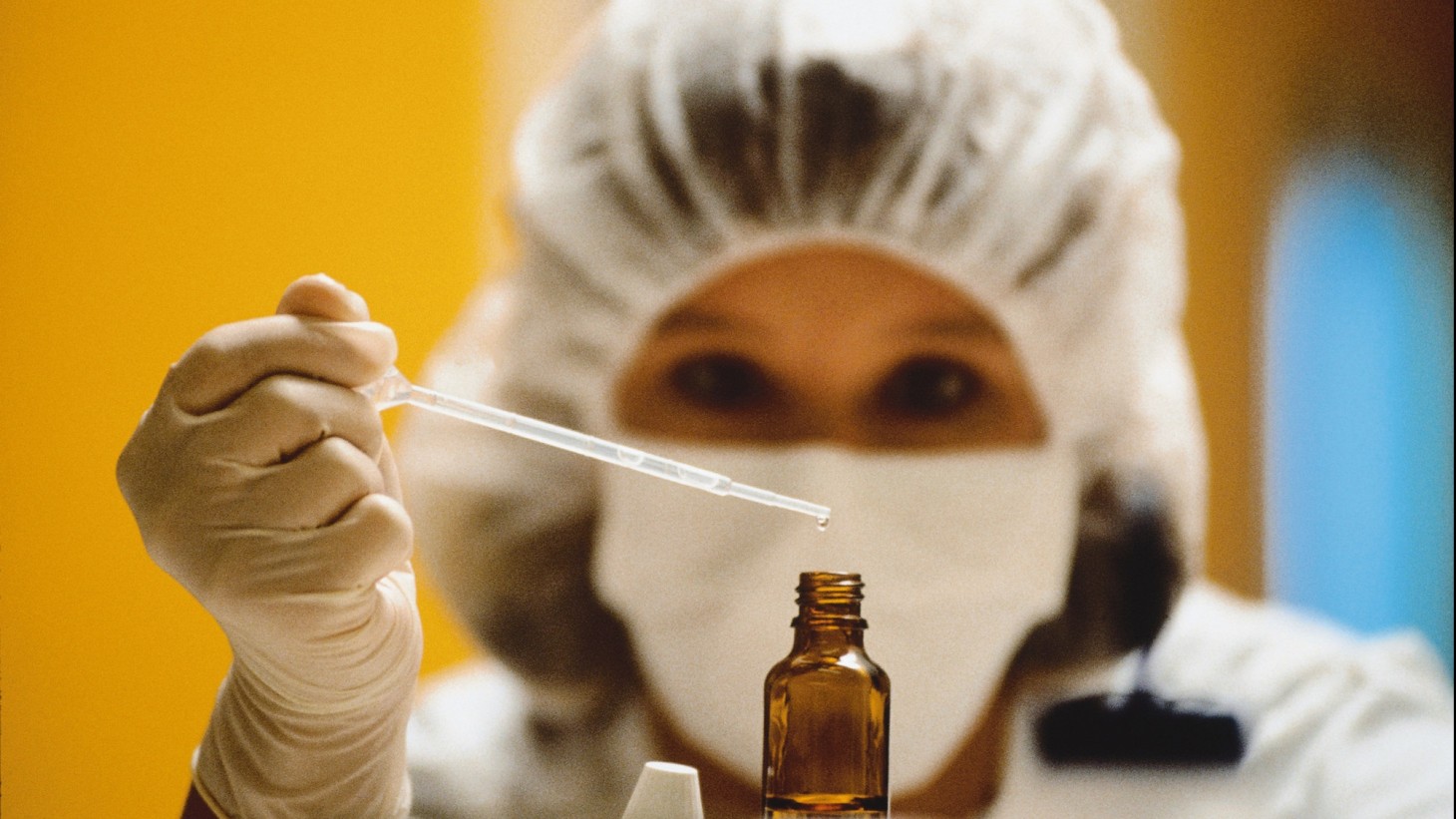 lab worker holding a pipette over a bottle 